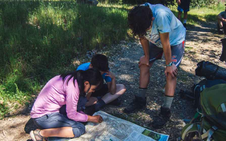 three outward bound students take a break from backpacking to examine a map